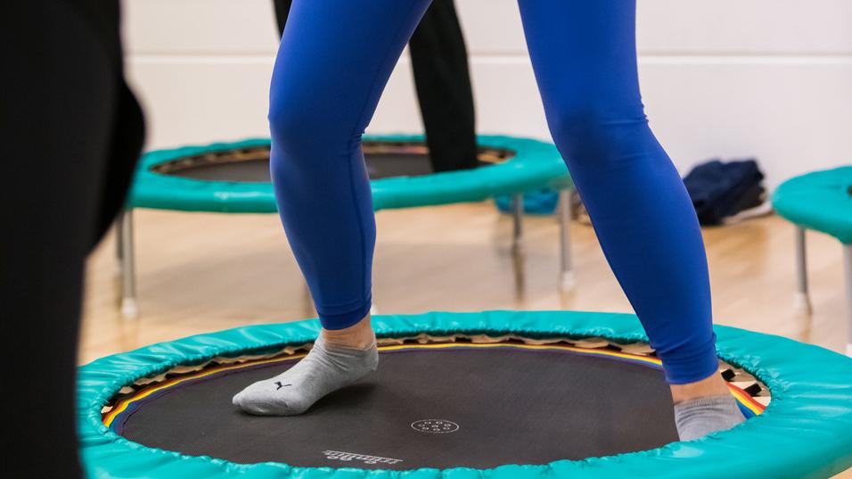 Eine Frau in blauer Sportkleidung springt auf einem Trampolin in einem Fitnessraum.